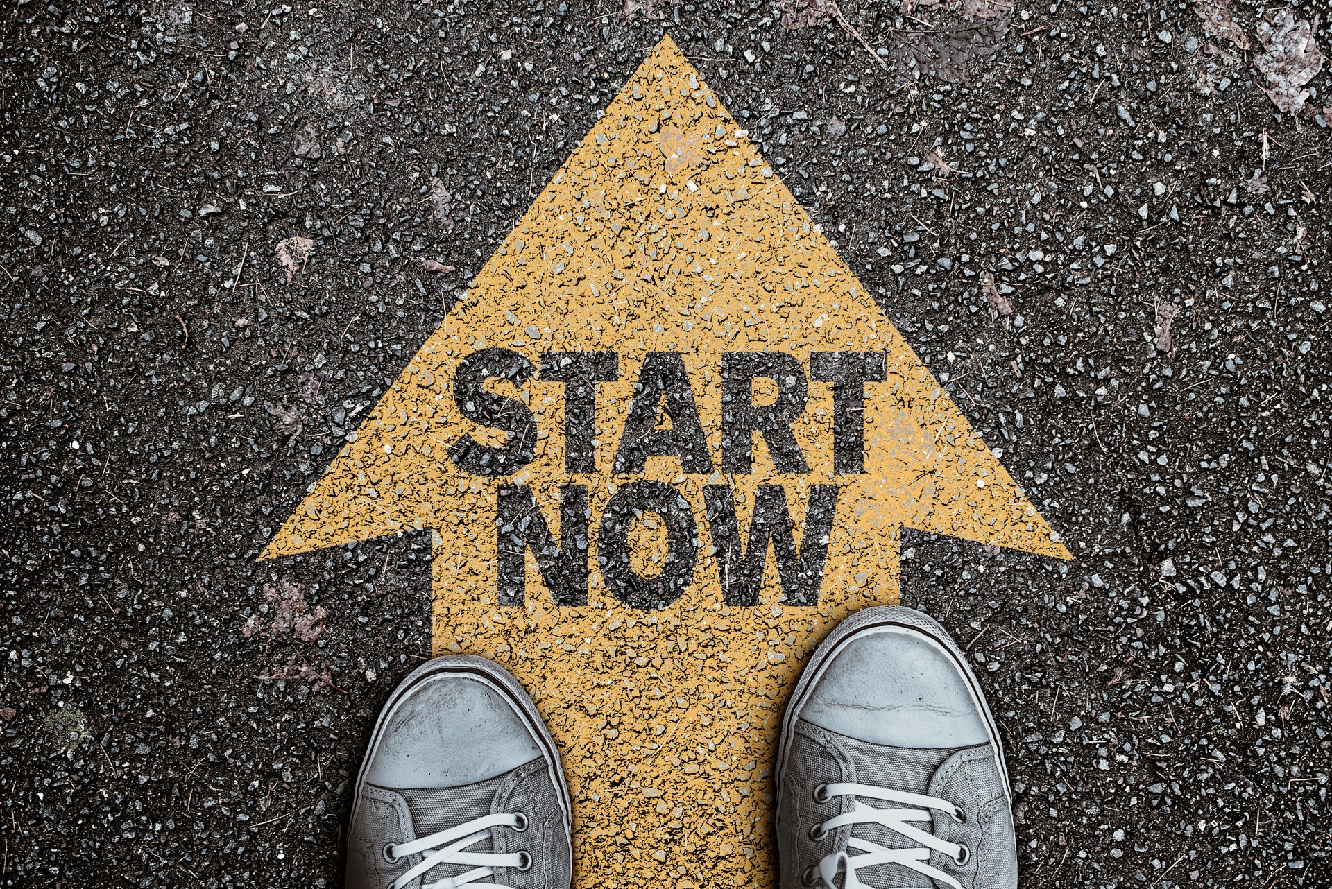 high angle view of person standing on arrow marking on asphalt, road with text START NOW